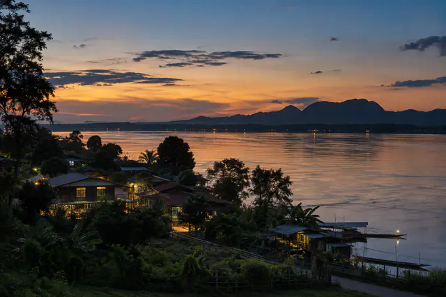 ชุมชนริมแม่น้ำโขงยามเย็นกับแสงจากบ้านเรือนและสายน้ำอันสงบ